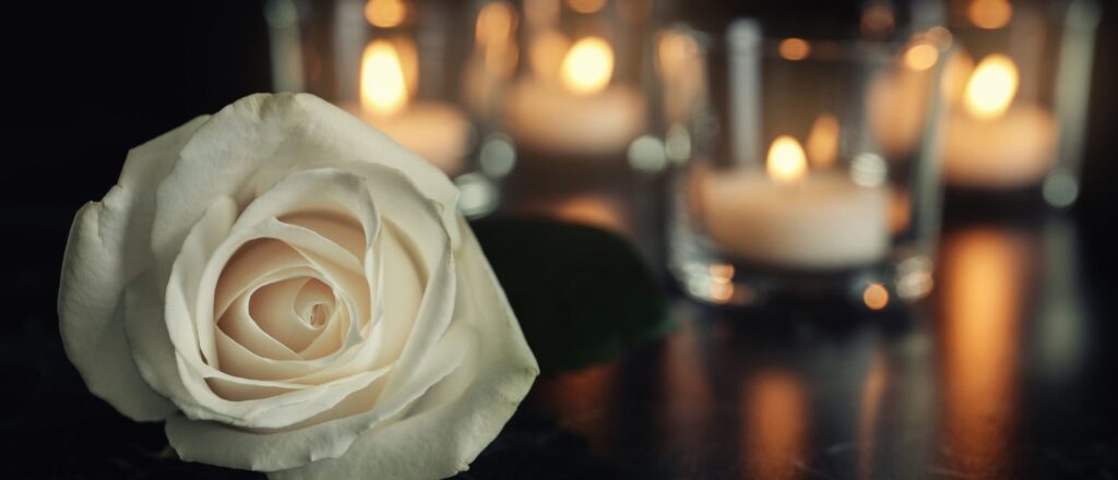 White,Rose,And,Blurred,Burning,Candles,On,Table,In,Darkness,