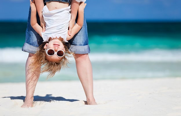 87 Funny July Quotes for a Happy and Hilarious Summer Month A small girl with sunglasses held upside down by an adult on the beach.