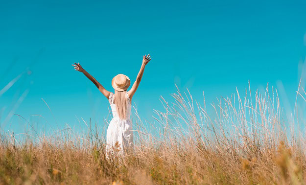 125 Positive Quotes About Life to Brighten Your Day Woman in a field stretching her arms towards the blue sky.