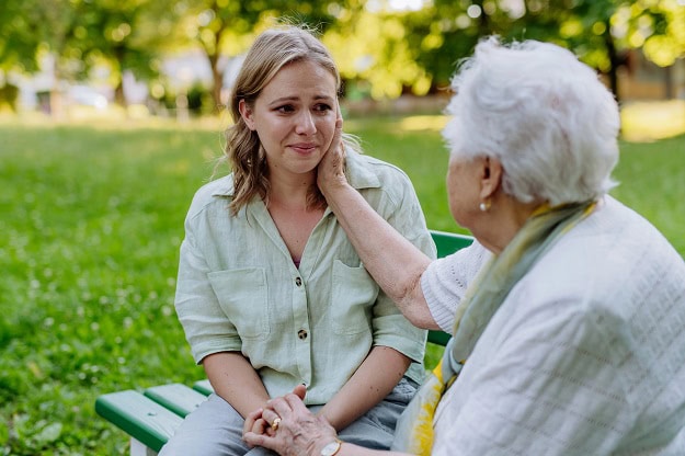 120 Grief Quotes to Uplift, Comfort and Help You Heal An older woman comforting a sad young woman while they sit on a park bench.