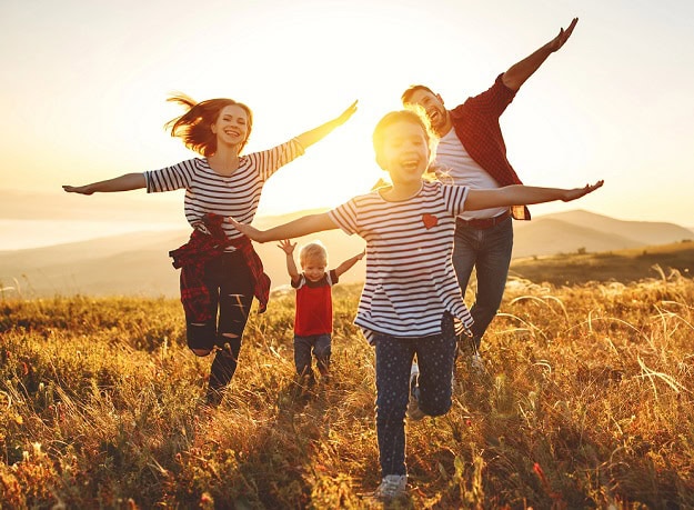 83 Funny Family Quotes: Relatable and Hilarious Humor A happy family running towards the camera in a field of grass with their arms stretched out imitating airplanes.