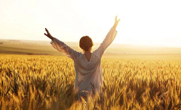 125 Inspirational Quotes for Women to Motivate and Empower You A woman in a field in summer with her arms stretched towards the sky.